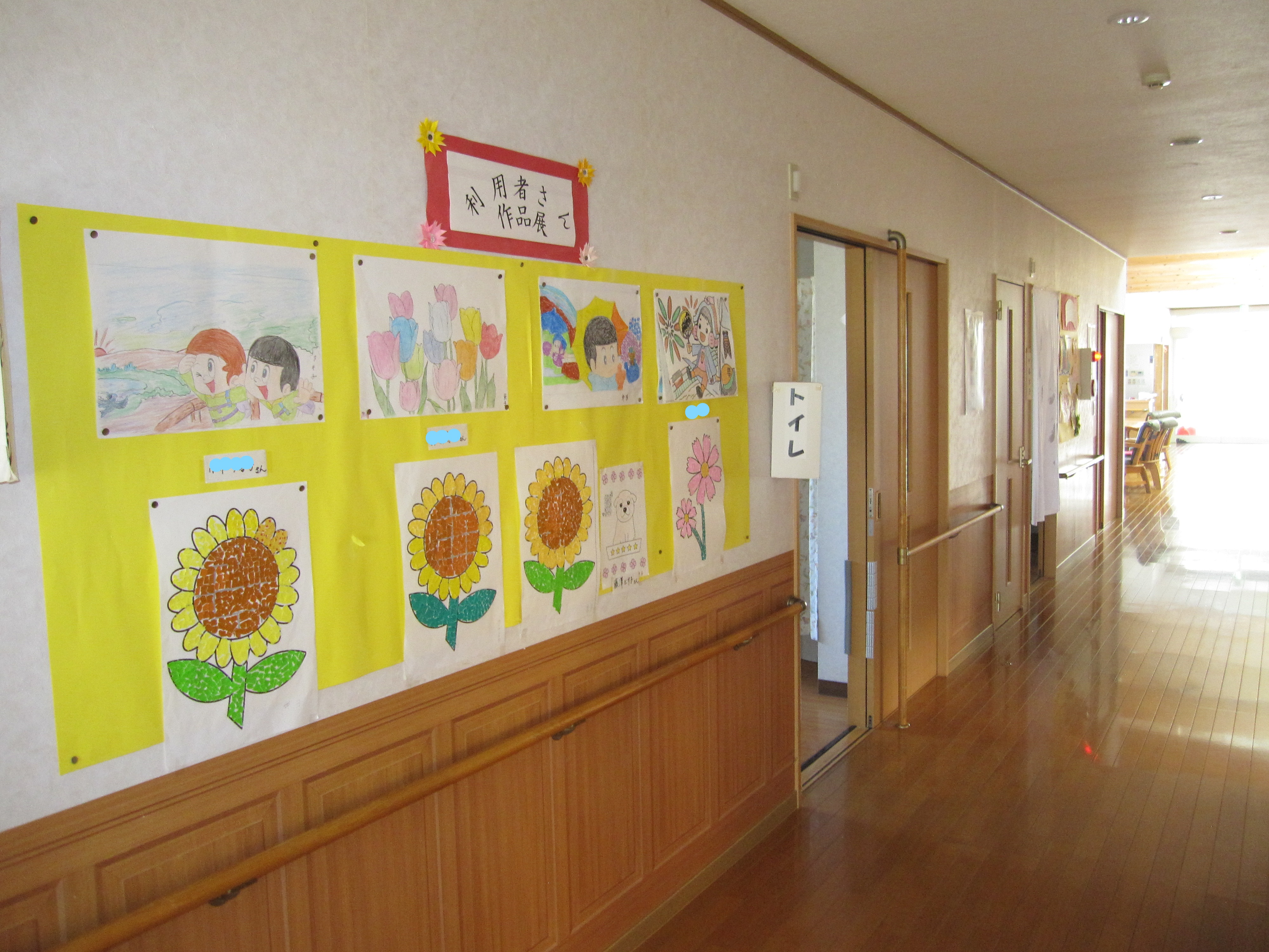 廊下に展示された入居者作品。黄色いパネルに向日葵などの絵画が飾られている。