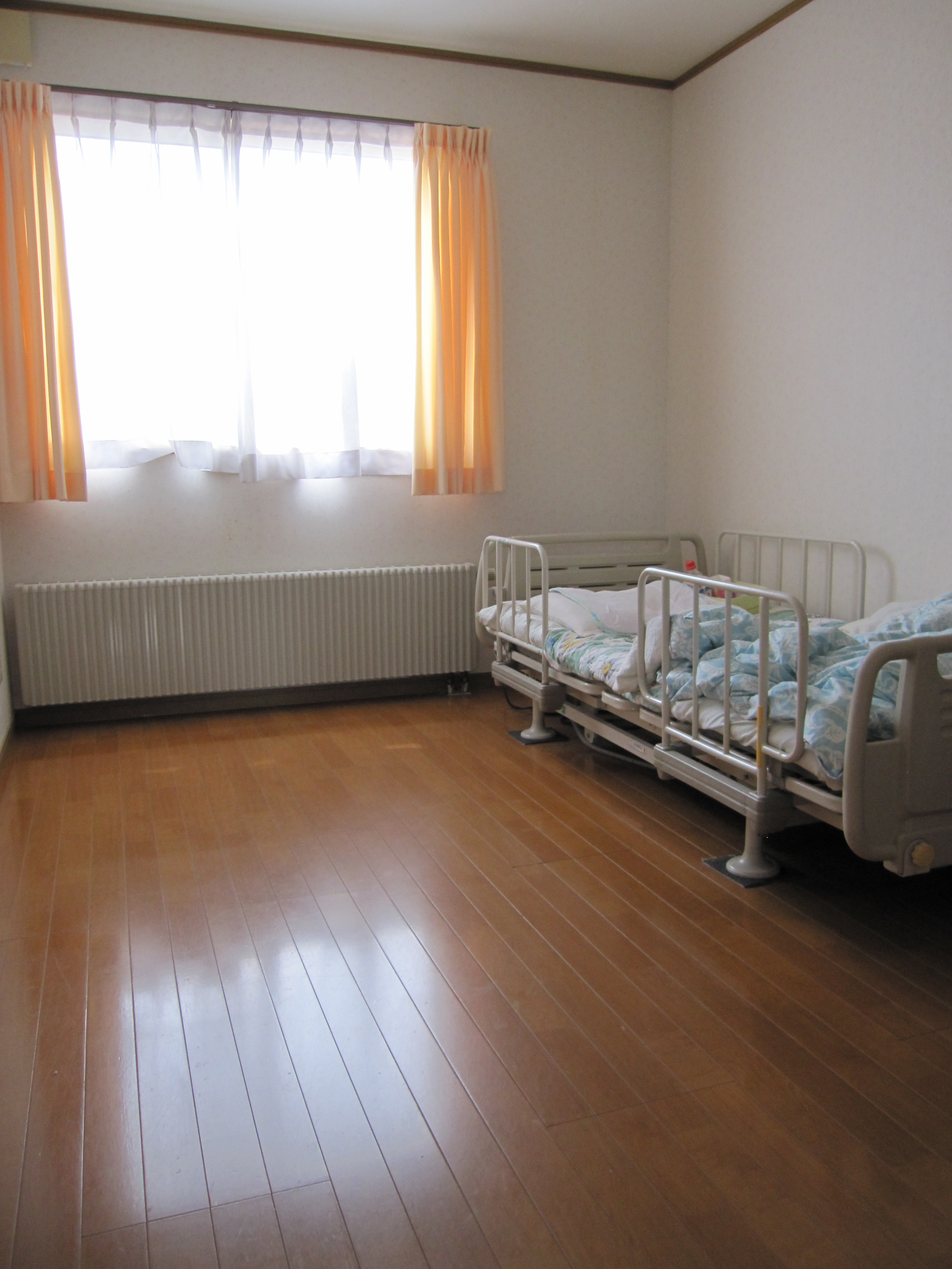 介護用ベッドが配置された明るい居室。窓からの採光が良好。
