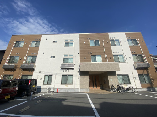 介護施設の建物外観。茶色と白の外壁、複数の窓、玄関エントランスが見える3階建て
