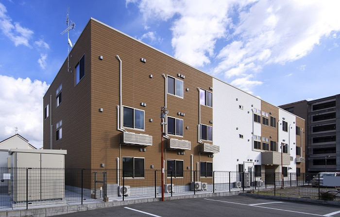 介護施設の建物外観。茶色と白の外壁が特徴的で、複数の窓が配置されている。