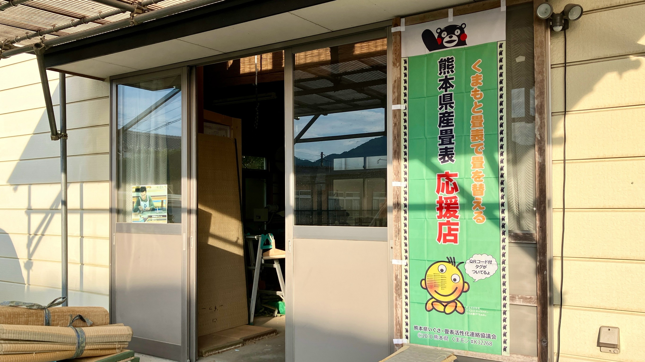 くまモンが描かれた緑色の熊本県産畳表応援店のぼり旗が堂々と掲げられた佐藤畳工業の仕事場作業場入り口の写真｜群馬県桐生市菱町