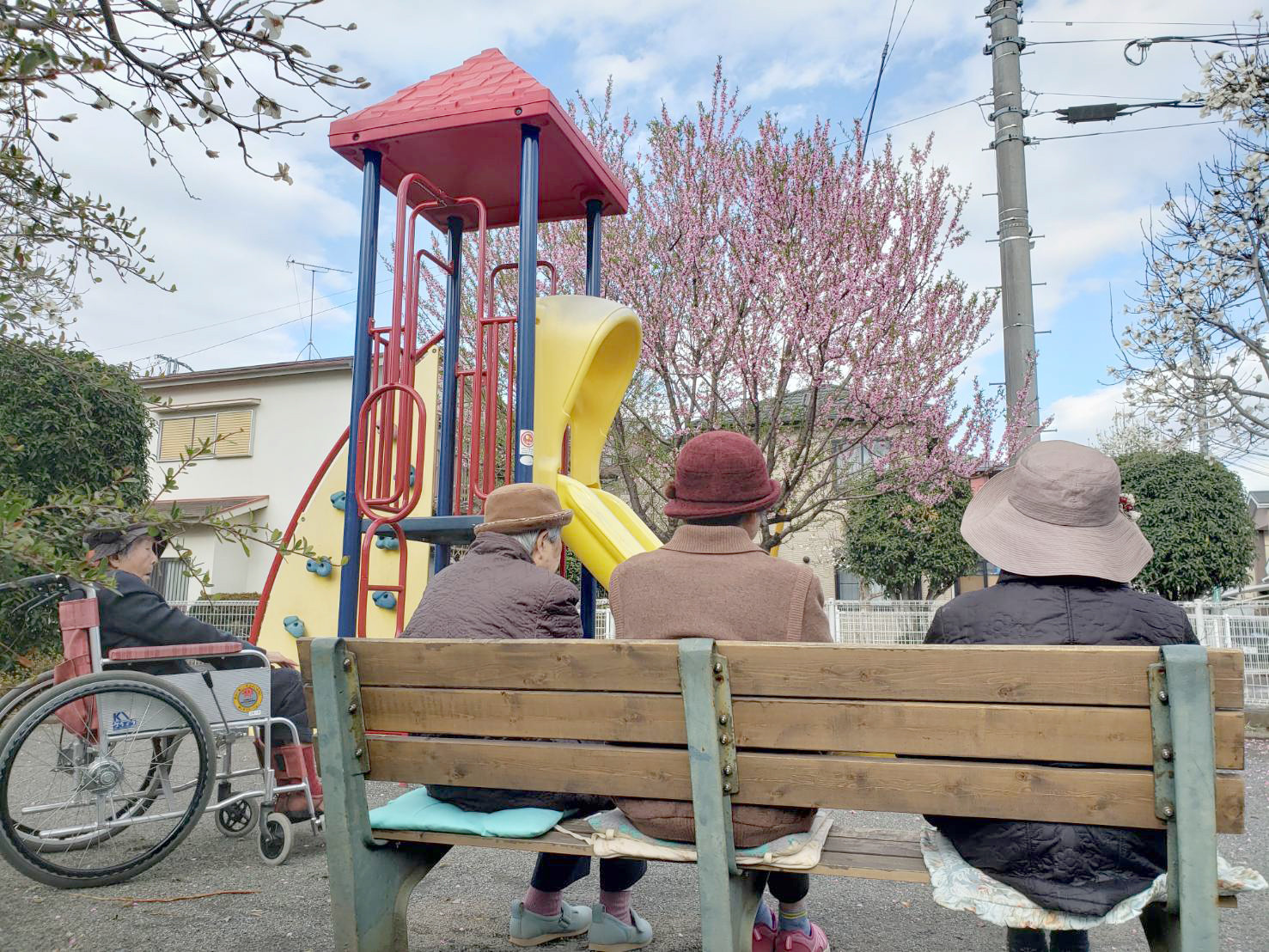 介護施設の入居者らが屋外の遊具前でベンチに座って過ごす様子