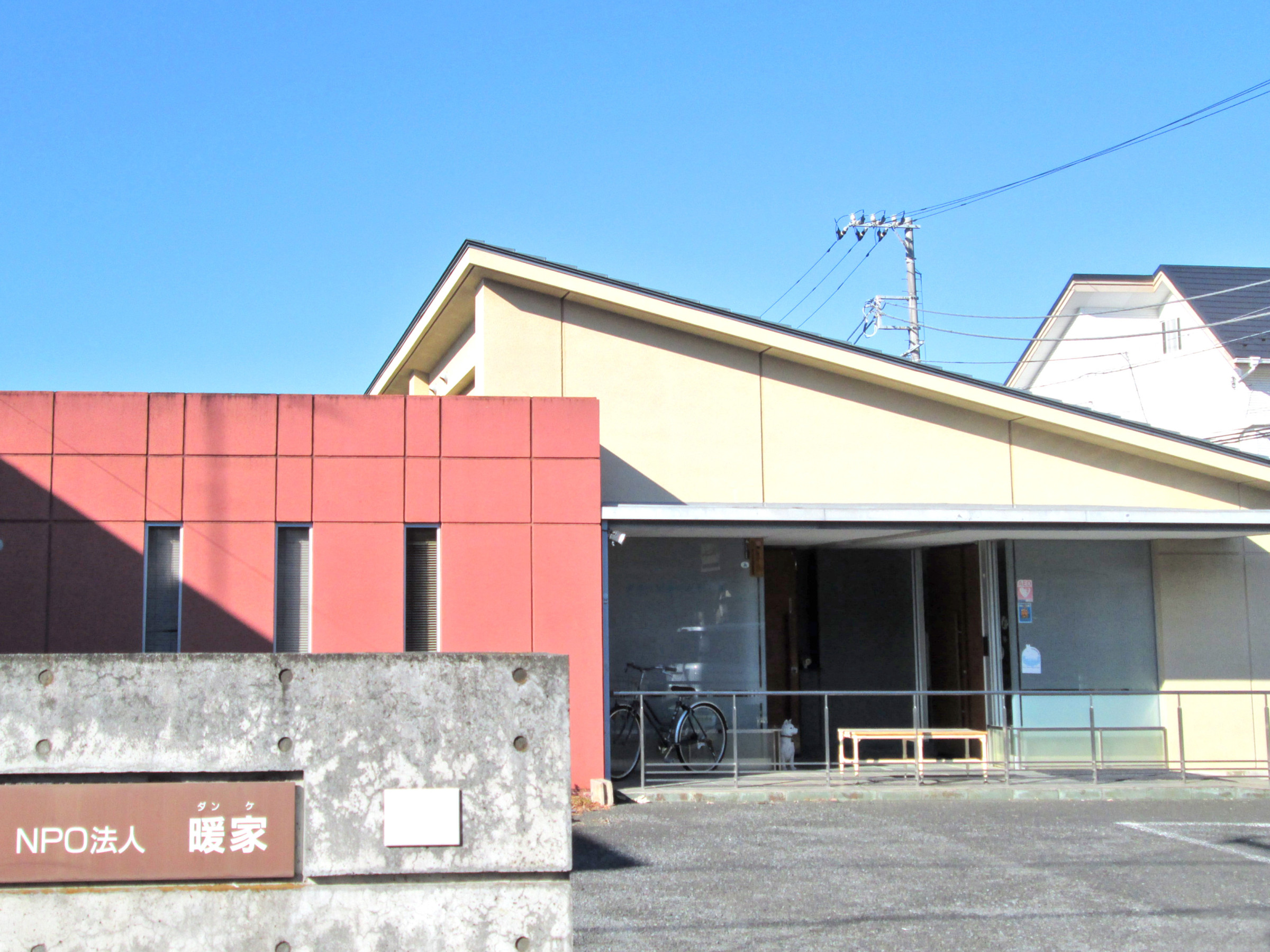 赤と白の外壁の介護施設の建物外観。NPO法人施設の看板が見える。