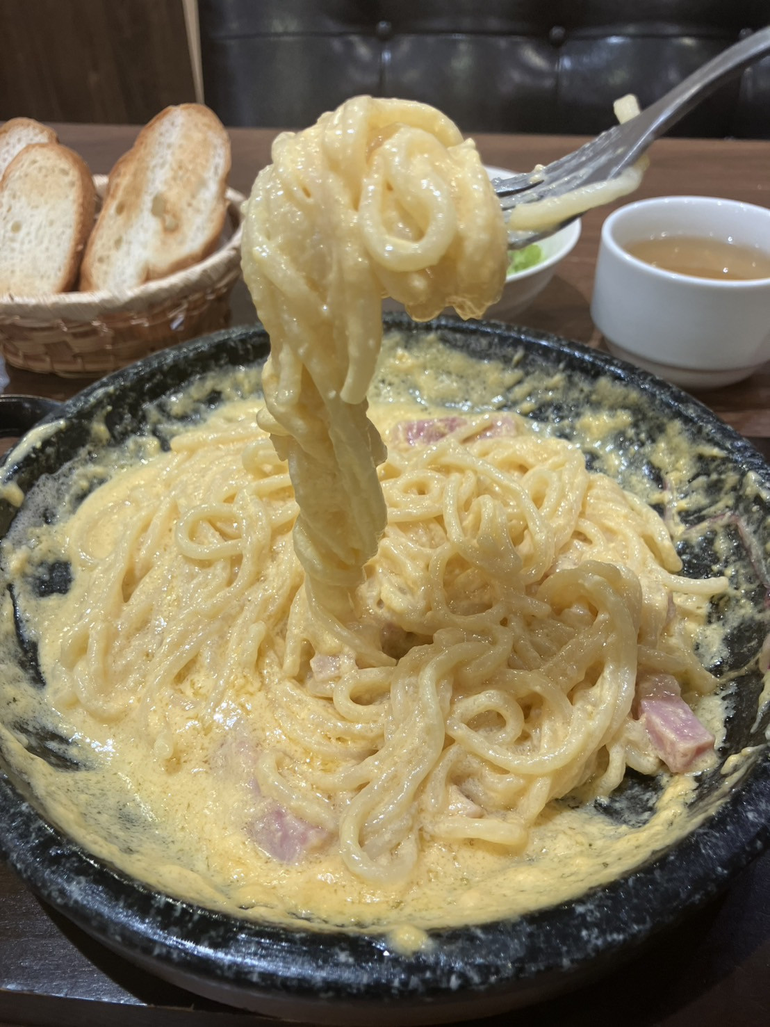 濃厚なソースが絡んだ石焼きカルボナーラの麺を持ち上げた完成写真。別料金のパスタセット付きの提供例