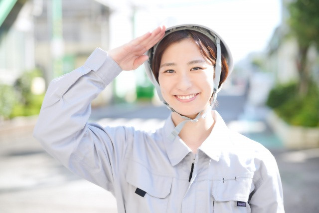 笑顔で敬礼する作業服の女性