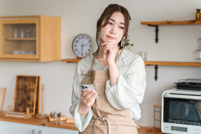 キッチンで考え事をするエプロン姿の女性