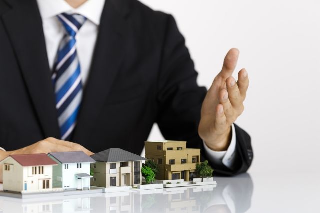 住宅模型を使って説明する不動産売買業者のイメージ