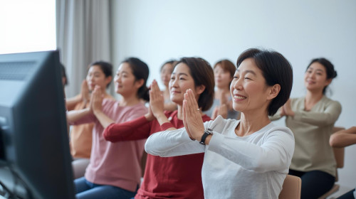 大きなモニター画面をみて椅子ヨガしている４０代から５０代女性１０名日本人・長袖・笑顔.jpg