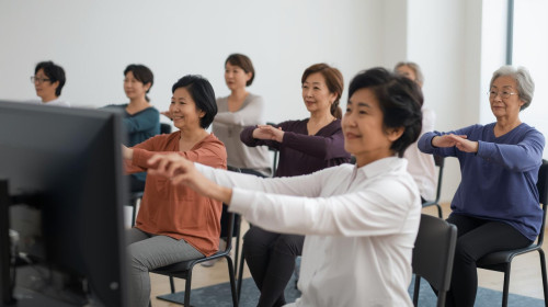 大きなモニターみながら、椅子ヨガしている60代綺麗なおば様方10名日本人・長袖・笑顔.jpg